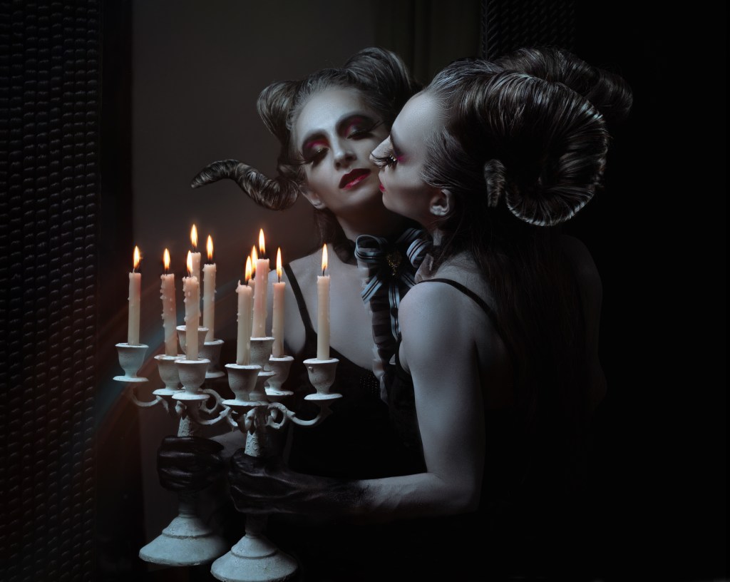 Joanne Froggatt dressed as a beautiful horned Halloween monster, looking into a mirror and holding a candle in the dark